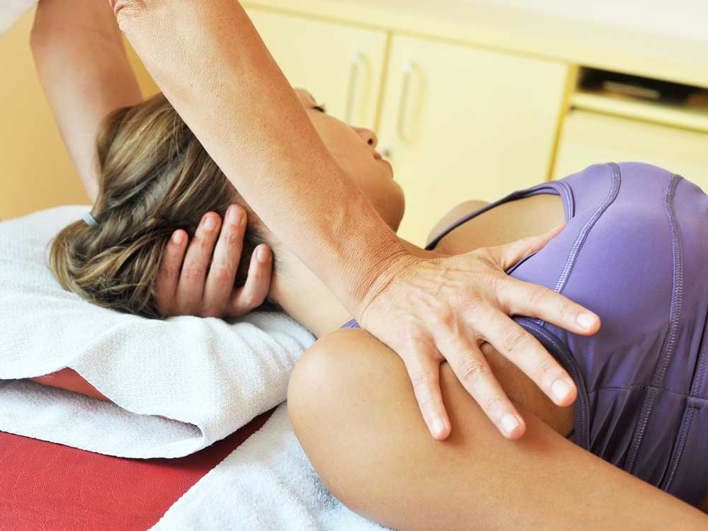 Behandlung einer liegenden Patientin durch eine osteopathisch arbeitende Therapeutin mit Fokus auf Schulter und Nacken